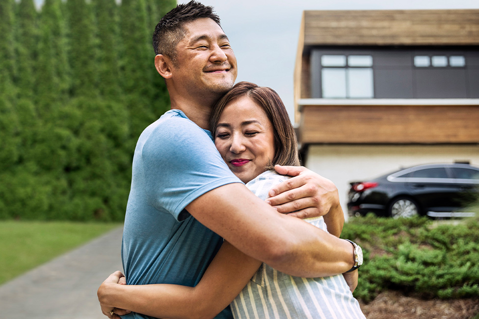 middle aged Asian couple hugging happily in front of their new home
